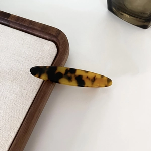 Detail of tortoiseshell acetate hair clip with leopard pattern on a wooden tray