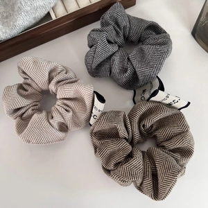 Close-up of three knitted scrunchies with herringbone pattern and brand labels in warm tones