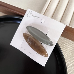 Set of two oval hair clips in muted green and marble amber on a display card