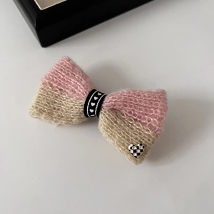 Détail d'une barrette nœud tricoté rose et beige avec cœur à damier et texture en laine