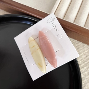 Close-up of two marble-textured oval hair clips in beige and pink on display card