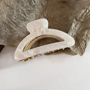 Detailed shot of pearlescent acetate hair claw clip with gold metal spring on paper