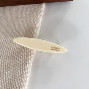 Close-up of cream oval resin hair clip with gold metal clamp and handmade engraving