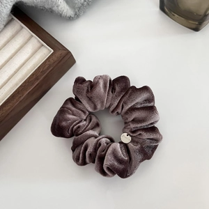 Detail of soft velvet scrunchie in coffee brown with a round silver metal tag