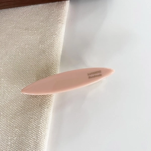 Close-up of pink oval resin hair clip with gold SANSHINE Handmade logo on fabric