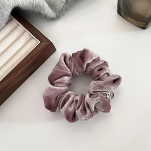 Macro detail of soft velvet scrunchie in dusty rose with a round gold metal tag