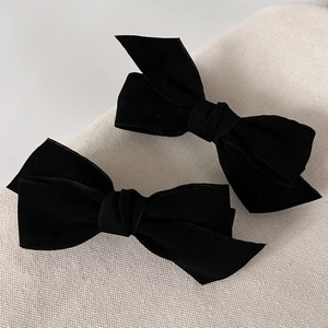 Elegant pair of black velvet bow hair clips for women on a textured neutral background