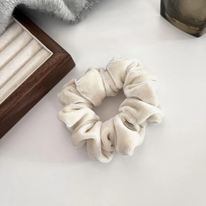 Close-up detail of soft velvet scrunchie in cream white with premium gold label and texture