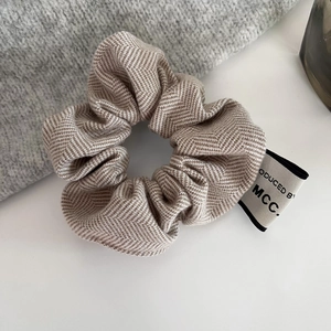 Close-up detail of herringbone twill fabric scrunchie with brand tag and coffee color texture