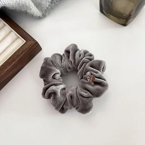 Detailed view of dark grey velvet scrunchie featuring a premium metal brand tag accessory