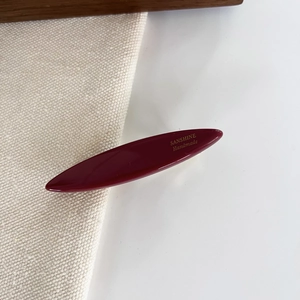 Macro view of a deep red oval resin hair clip with elegant gold handmade lettering