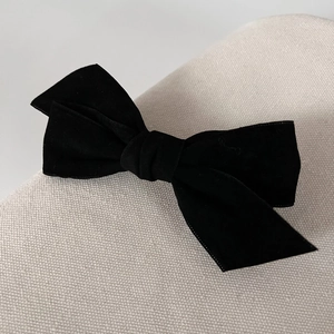 Close-up of black velvet bow hair clip with fine fabric texture on woven background
