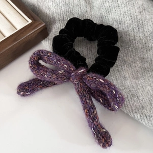 Close-up of a purple tweed knit bow and black velvet scrunchie on a wooden tray
