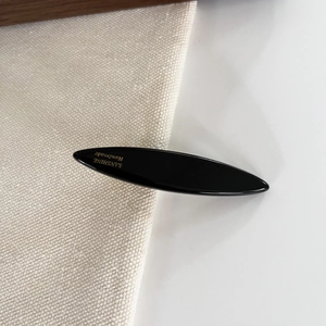 Detail view of a black handmade hair clip featuring a sleek oval shape and golden SANSHINE logo