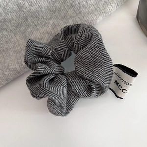Close-up of grey herringbone fabric scrunchie with brand tag on white surface