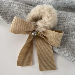 Detail of soft winter bow scrunchie with plush pearl decor on a cozy knit background