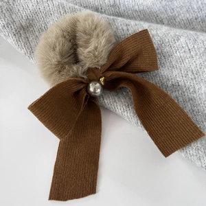 Detail of plush brown bow hair tie with pearl accent on cozy knitted sweater