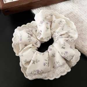 Détail d'un chouchou en dentelle fleurie crème avec motifs lavande et bords en dentelle