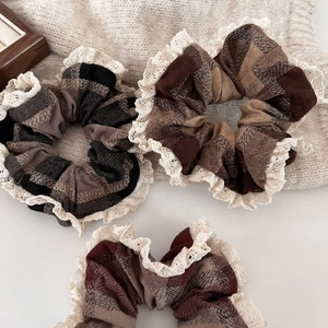 Close-up of three plaid scrunchies with white lace edges in hazel brown and red colors