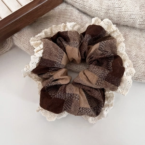 Detail of hazelnut brown plaid hair scrunchie with lace trim on a beige sweater