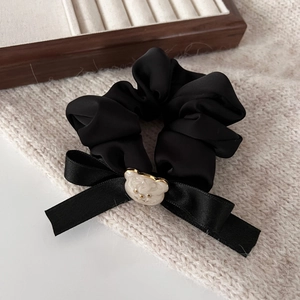 Détail d'un chouchou en satin noir avec nœud papillon et breloque ours de couleur crème