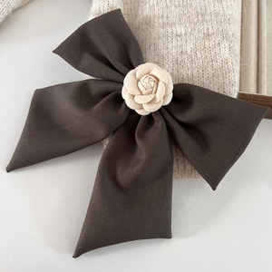 Détail d'un grand nœud à cheveux en satin marron avec une fleur de camélia crème
