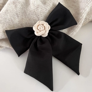 Détail d'un nœud papillon en satin noir avec camélia crème sur un clip à cheveux chic