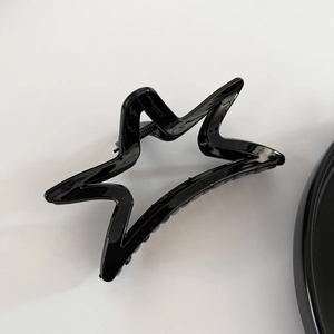 Détail d'une grande pince à cheveux étoile noire brillante avec un design ajouré