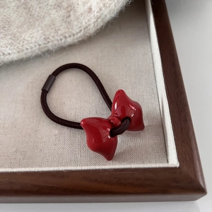 Detailed macro view of a glossy red resin bow hair tie on a high-elastic brown band