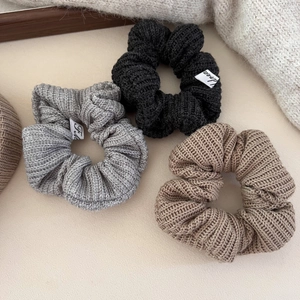 Trois chouchous en tricot noir, gris foncé et avoine avec étiquettes tissées