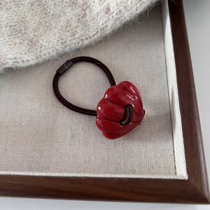 Close-up of a red shell-shaped resin charm on an elastic hair tie in a wooden tray