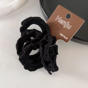 Detail of high-elasticity black ruffled scrunchies with brand tag on minimalist tray