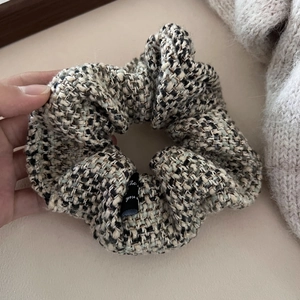 Detail of tweed scrunchie featuring woven texture and decorative black brand label
