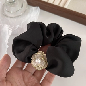 Detail of black satin hair scrunchie featuring camellia flower and pearl decoration