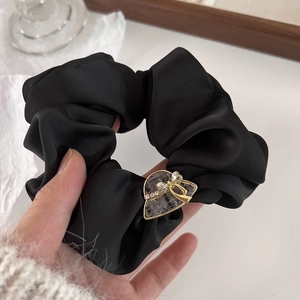 Detail of black satin scrunchie featuring a heart metal buckle with crystal accents