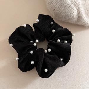Elegant black velvet scrunchie with white pearl accents on minimalist beige background