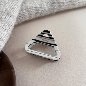 Détail de la pince à cheveux triangle en acétate avec rayures noires et blanches et logo