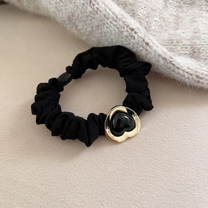 Elegant black heart hair scrunchie with golden metal trim on soft beige background