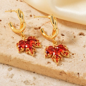 Elegantes pendientes de hoja de arce dorados con circonitas rojas sobre piedra beige
