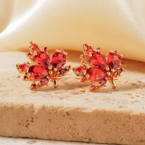 Detalle de pendientes de hoja de arce con circonitas rojas y baño de oro
