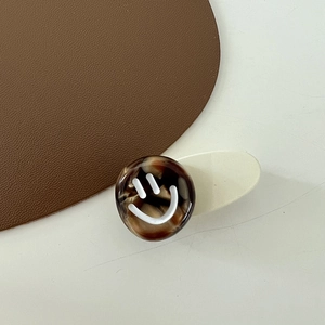 Detail of a minimalist smiley face flower hair clip with amber texture on a cream base