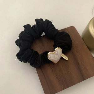 Detail view of a black scrunchie with a pearl heart charm and a gold handmade metal tag