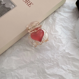 Detailed close-up of a small transparent hair claw clip with a glossy red heart on paper