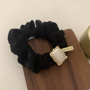 Detailed macro of black fabric scrunchie with pearl ornament and gold handmade tag