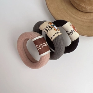 Three knitted teddy bear hair ties in pink, grey and black colors on white surface