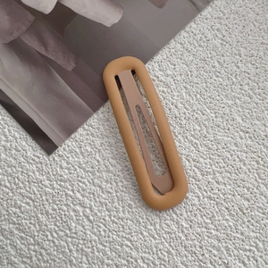 Detail of minimalist matte mustard yellow and beige oval hair clip on textured surface