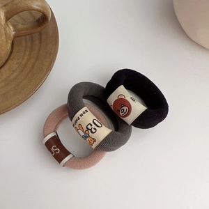Detailed shot of three elastic bear hair ties in black, grey, and pink on a white table