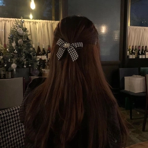 Houndstooth bow hair clip with white pearl detail on brown hair in cozy setting