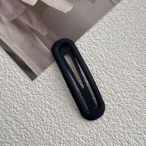 Close-up of matte black metal oval hollow hair clip on a textured white surface