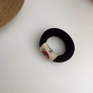 Detail of black plush hair tie featuring a white bear label and soft towel texture